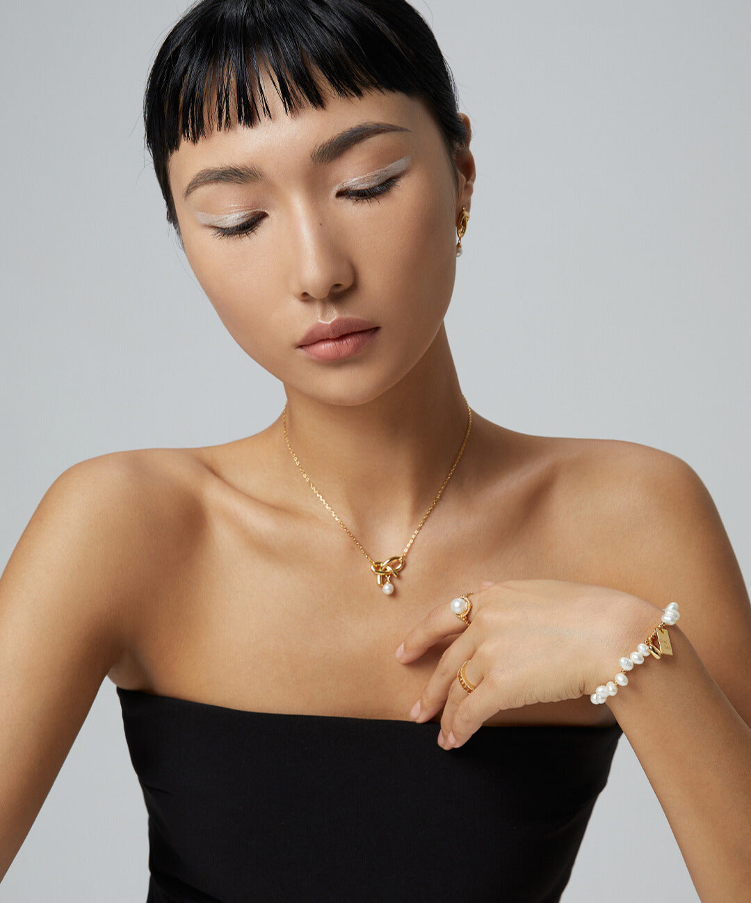 A woman in a black dress accessorized with gold jewelry, featuring gold pearl knot necklace.