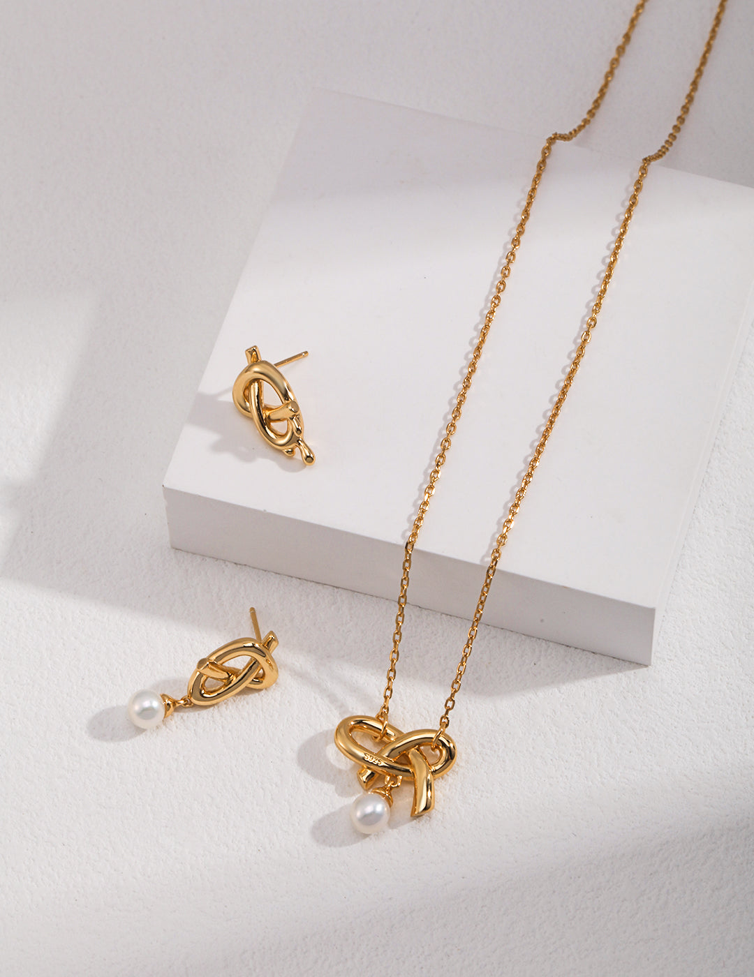 A stunning gold necklace and earrings set featuring a beautiful gold pearl knot design.
