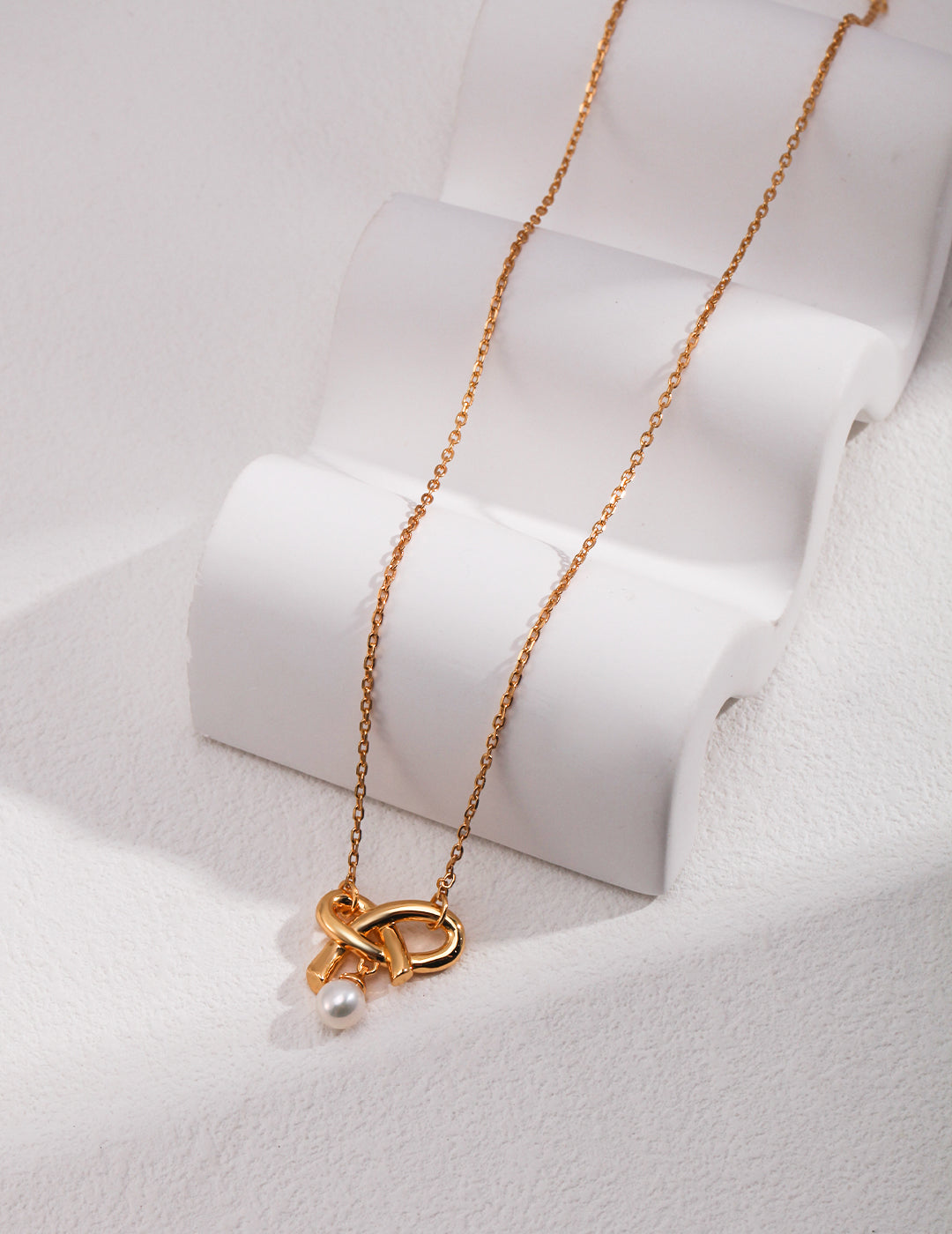 A luxurious gold necklace with a pearl knot pendant.