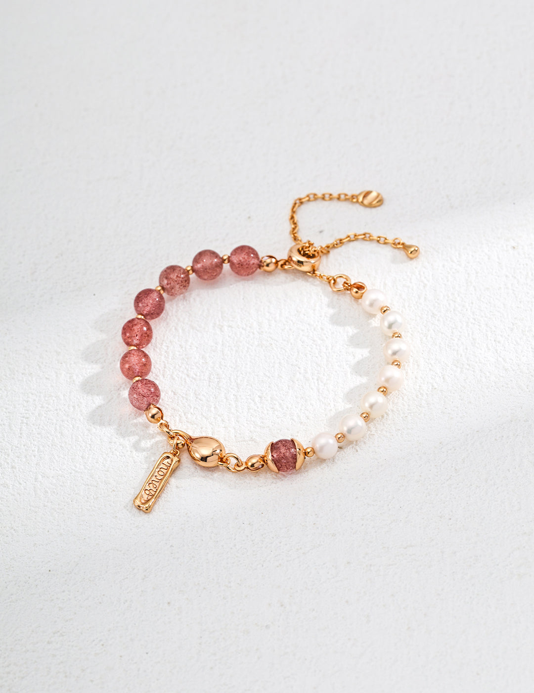 Beaded bracelet in pink and white, crafted from pearl and strawberry quartz, with a decorative gold charm.