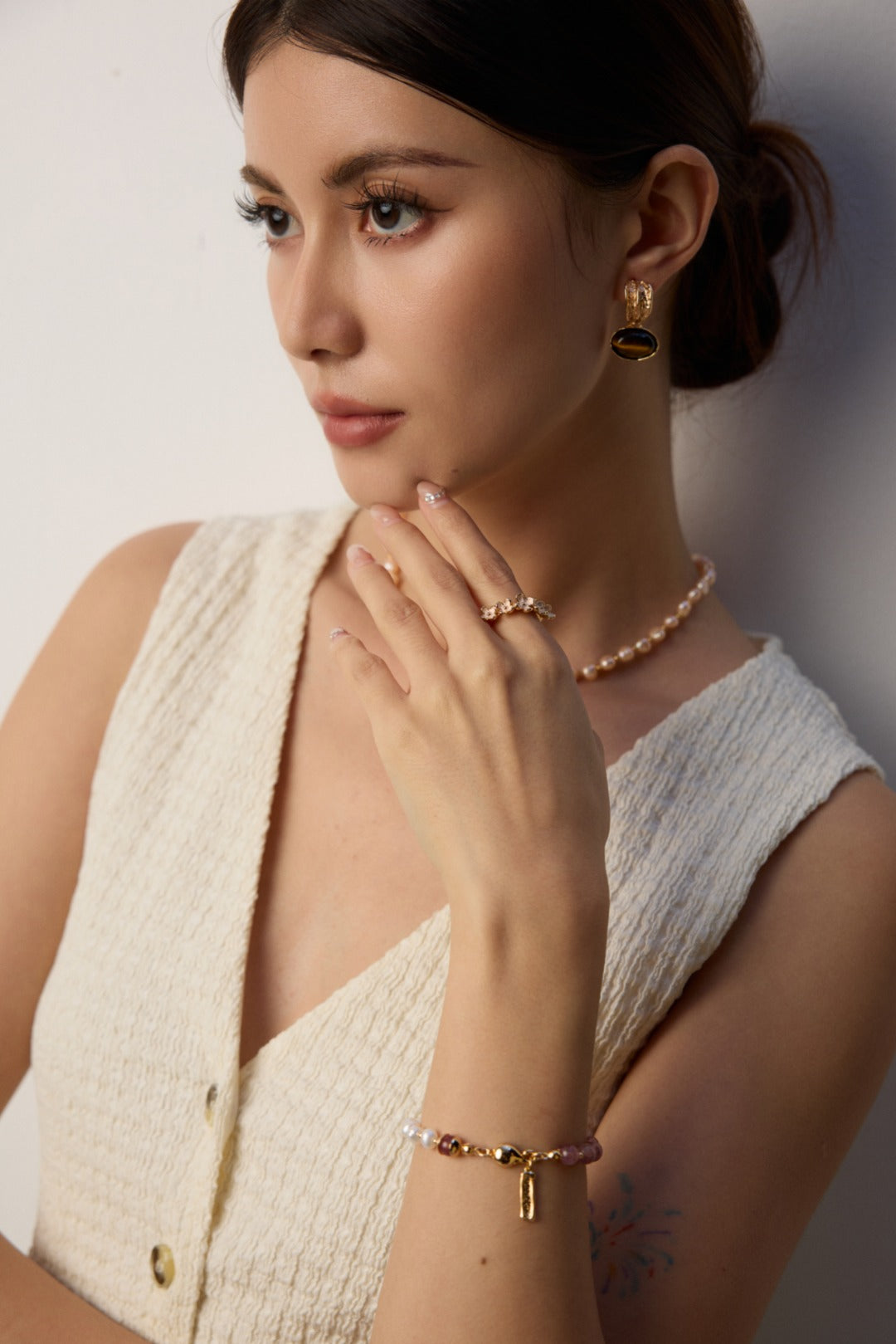 A woman dressed in a white shirt, showcasing a gold bracelet with pearl and strawberry quartz accents.
