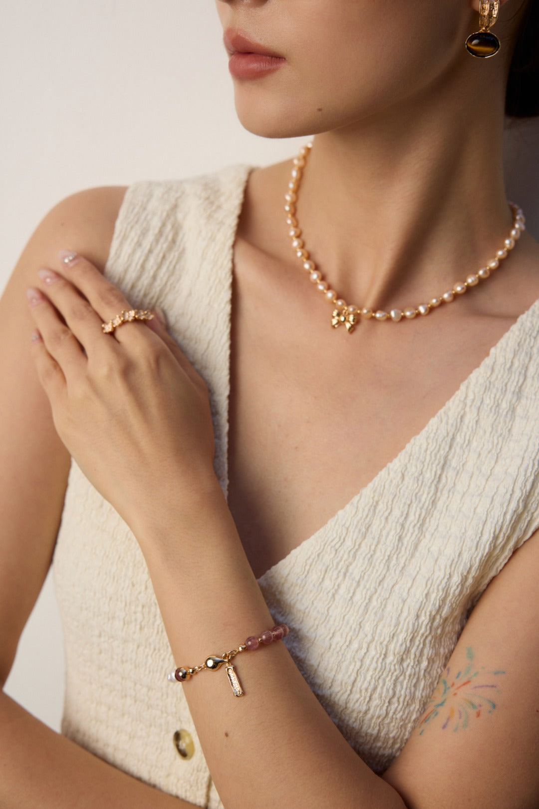 A woman dressed in white with a pearl necklace and a bracelet featuring pearls and strawberry quartz.