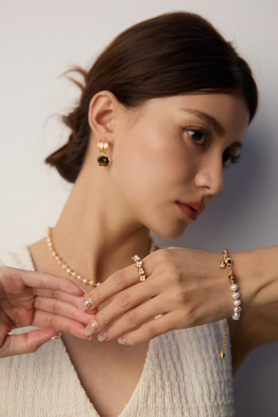 A woman in a white dress and pearl necklace, wearing a bracelet made of pearls and strawberry quartz.