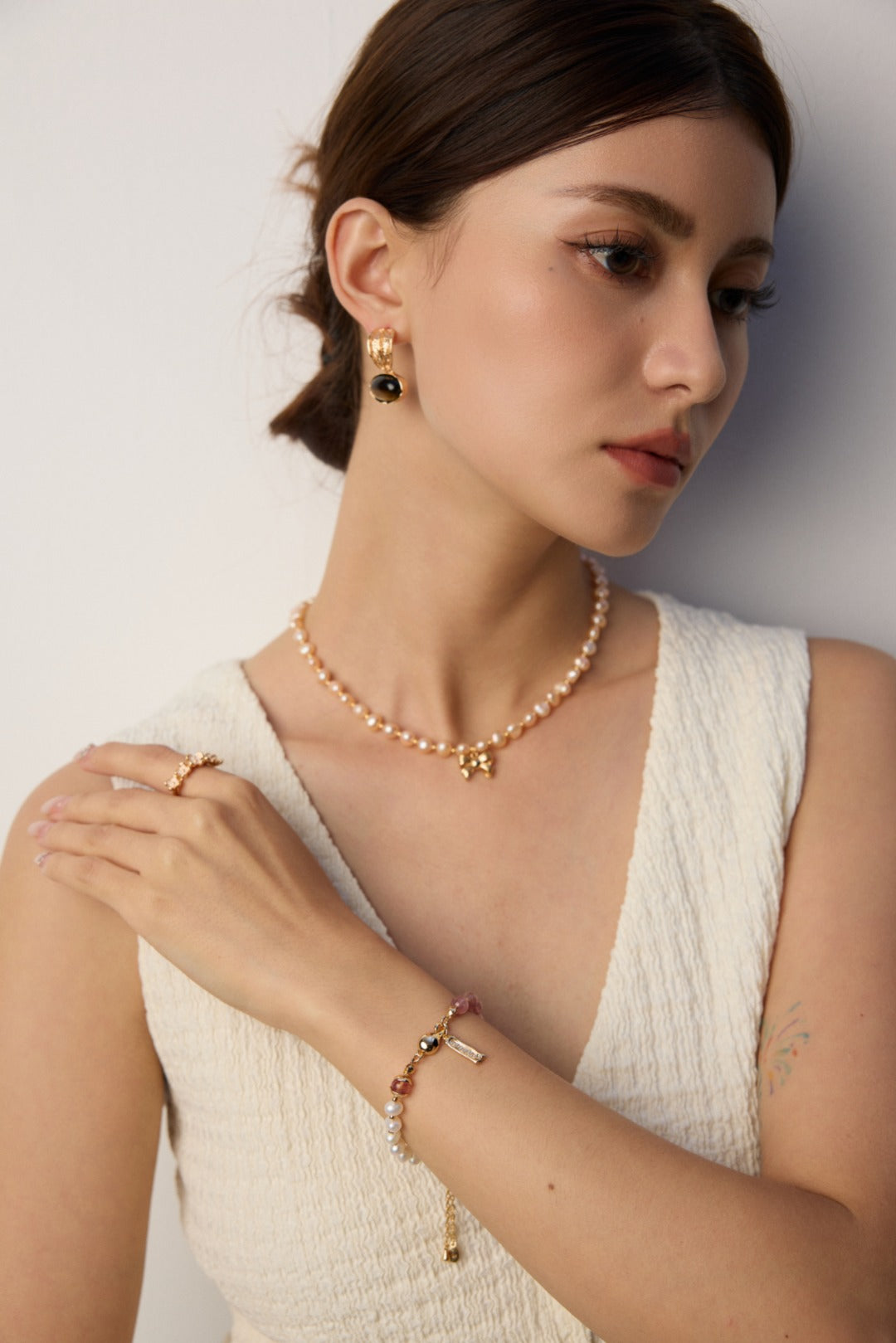 A woman dressed in white with a pearl necklace and a bracelet featuring pearls and strawberry quartz.