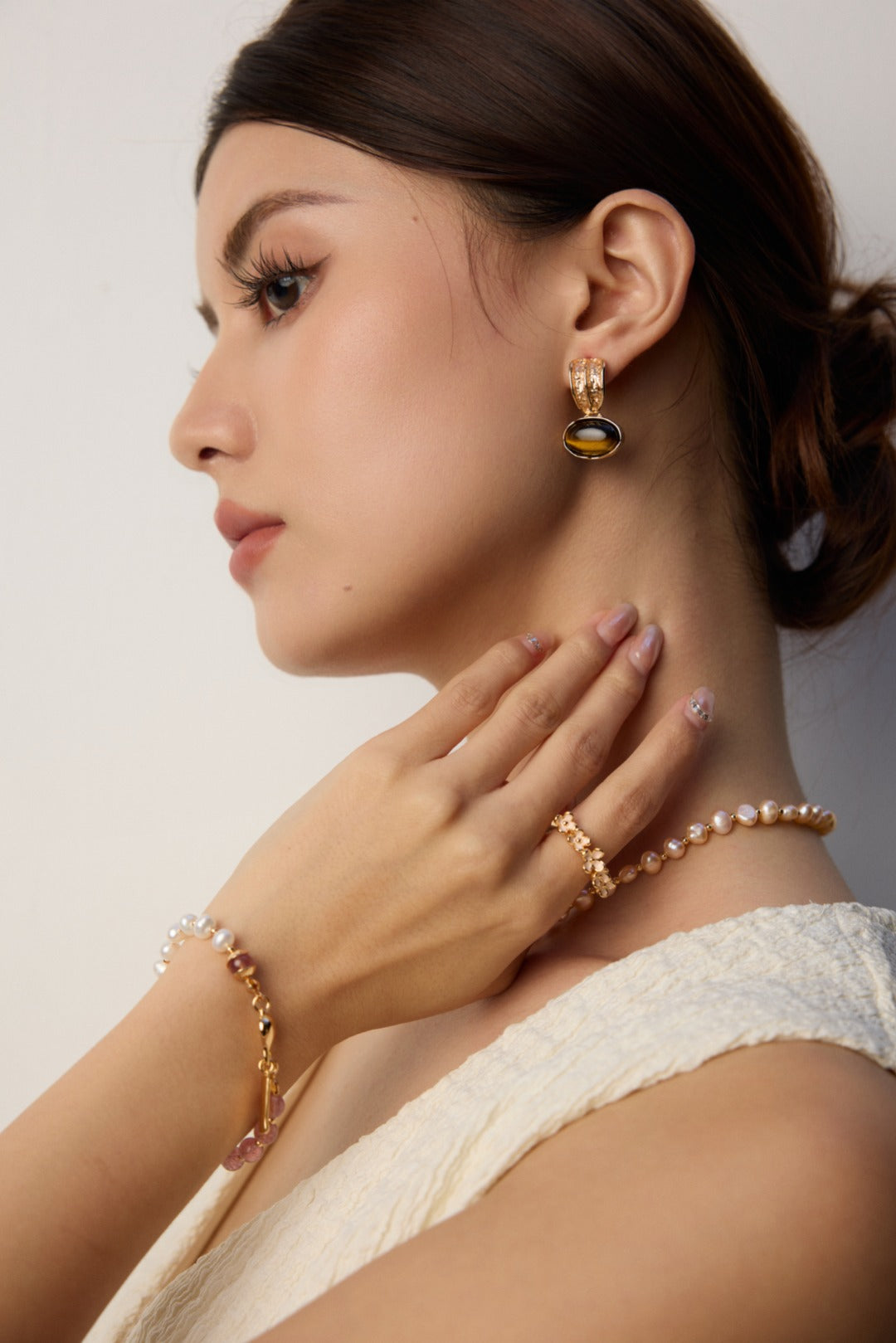 A woman in a white dress, accessorized with a pearl and strawberry quartz necklace and bracelet.
