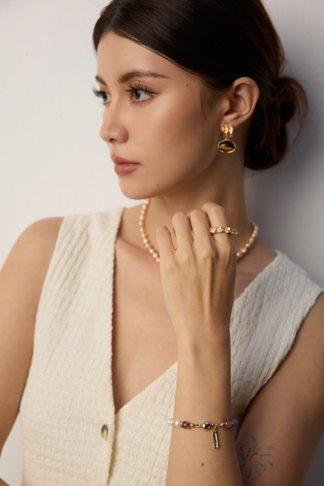 A woman with a pearl necklace and white shirt, showcasing a bracelet of pearls and strawberry quartz.