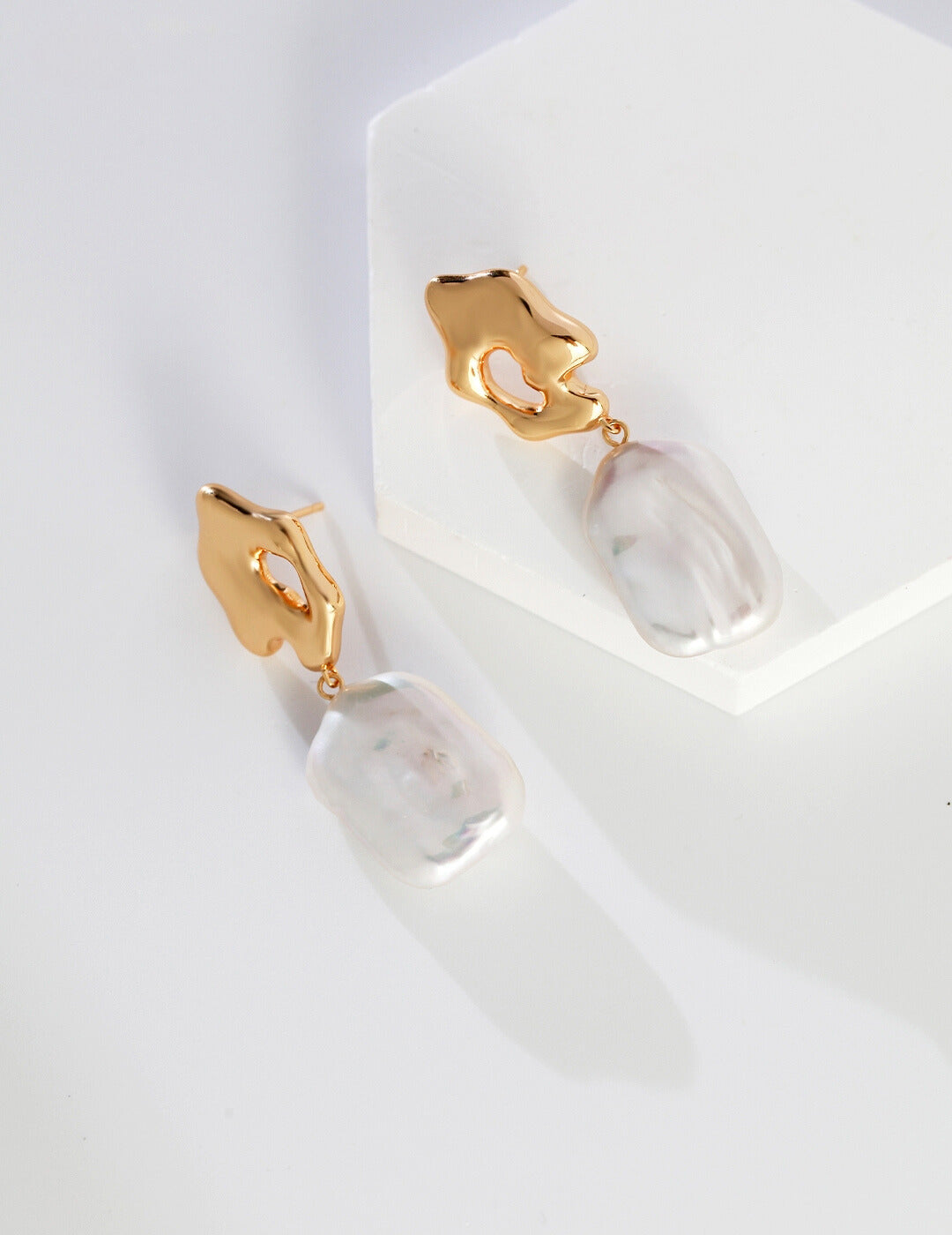 Gold plated earrings on a white surface, showcasing the beauty of baroque pearls.