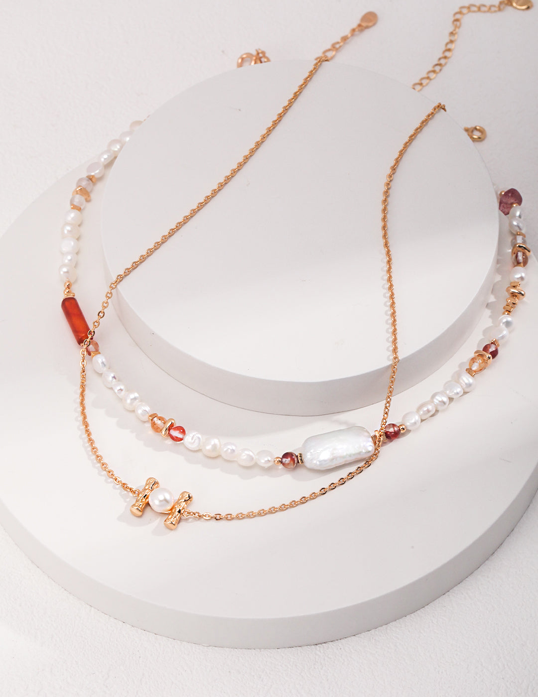 Gold chain necklace with freshwater pearls and strawberry quartz, layered with another gold necklace.