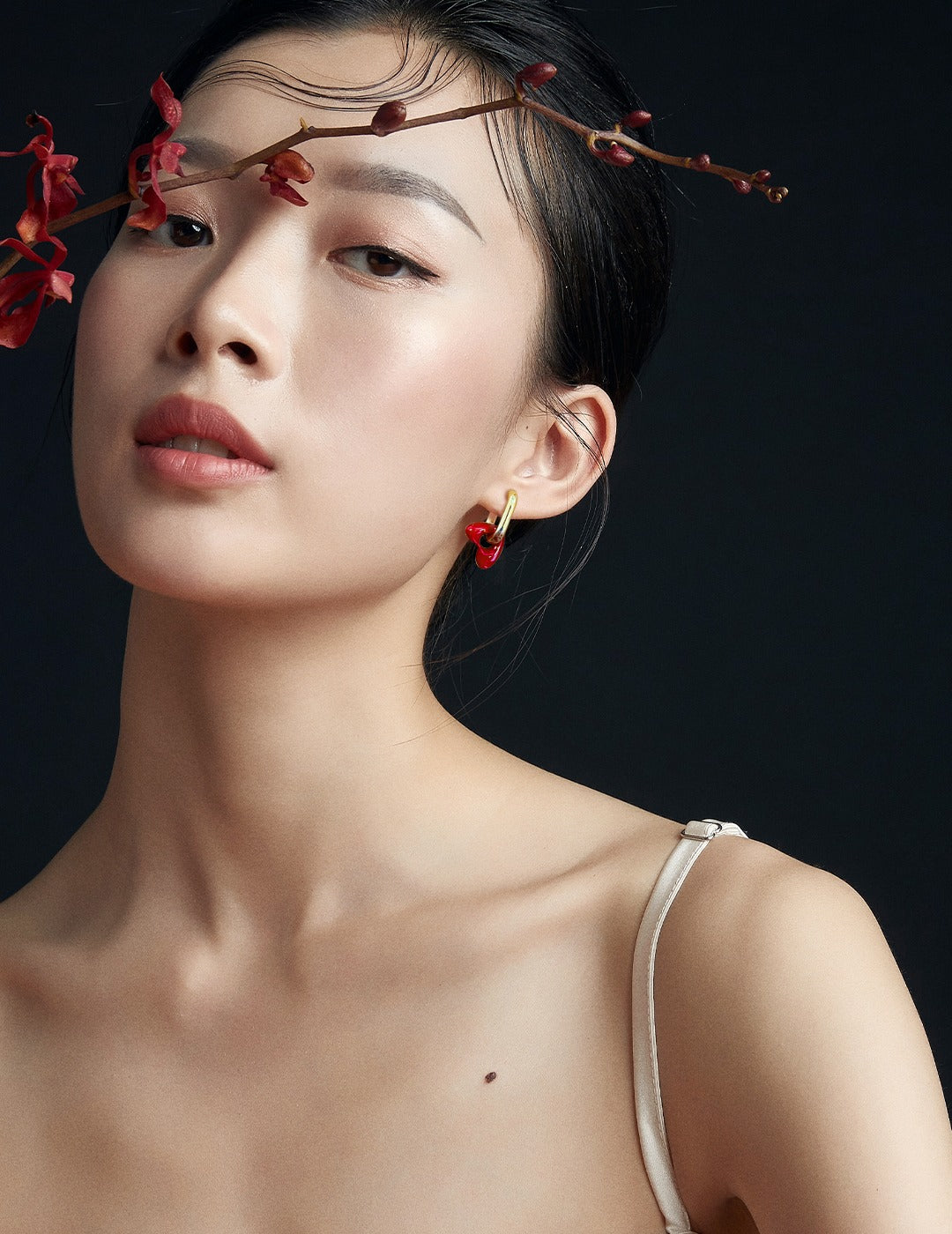 Model adorned with red flowers in hair, accessorized with gold plated hoops featuring red enamel hearts.