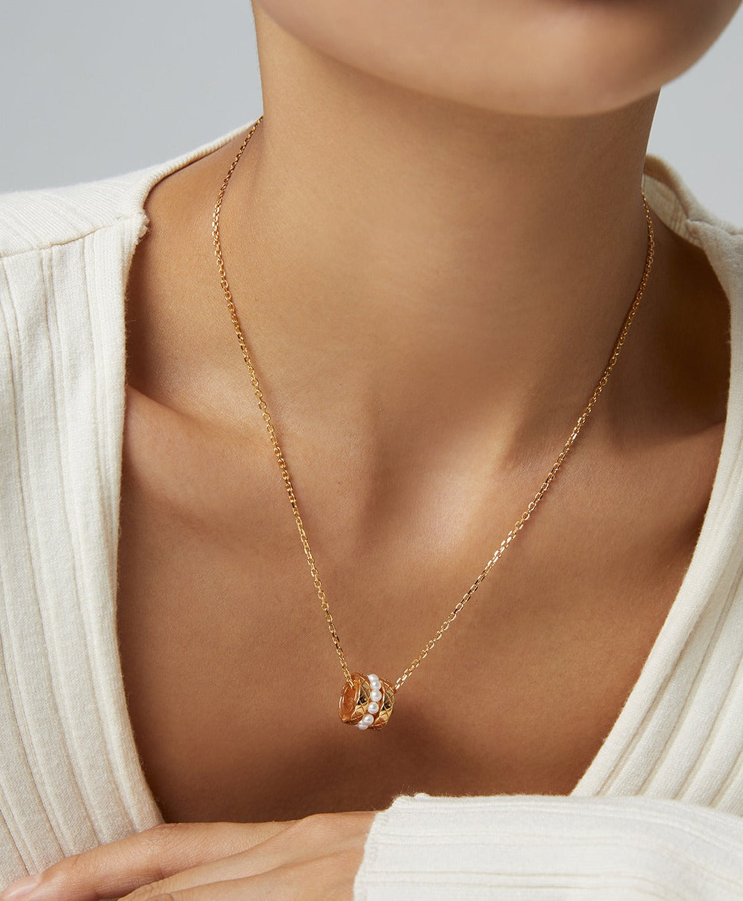A woman wearing a gold necklace with a gold pendant and pearl beads.