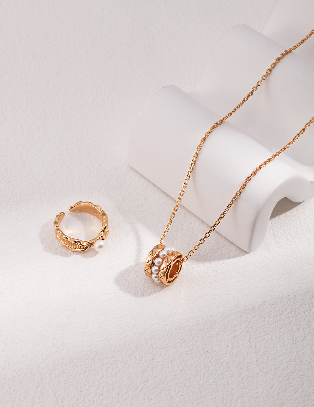 A stunning gold necklace and a ring, displayed on a white surface.