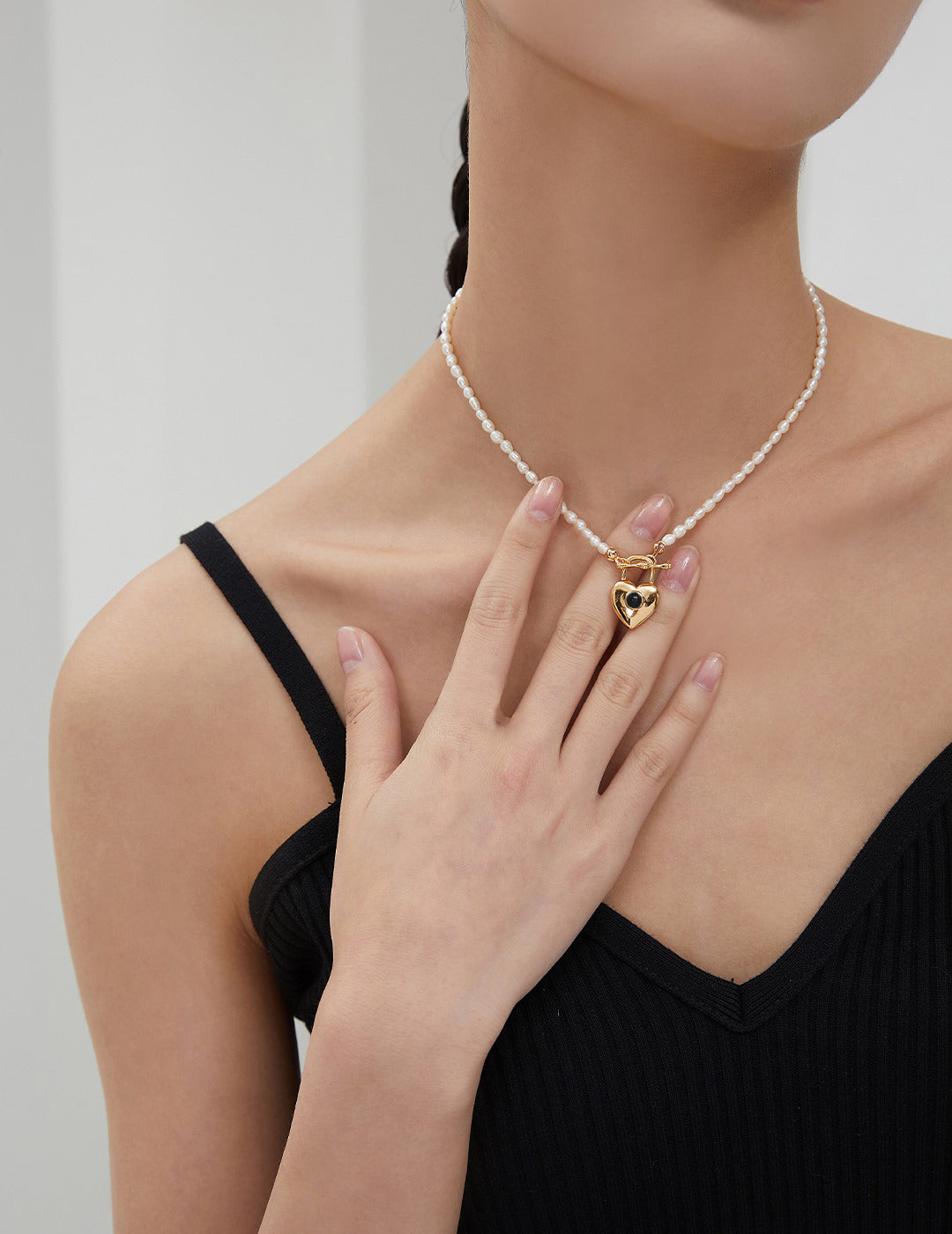 Woman wearing gold necklace with heart charm, touching her rice pearl necklace.