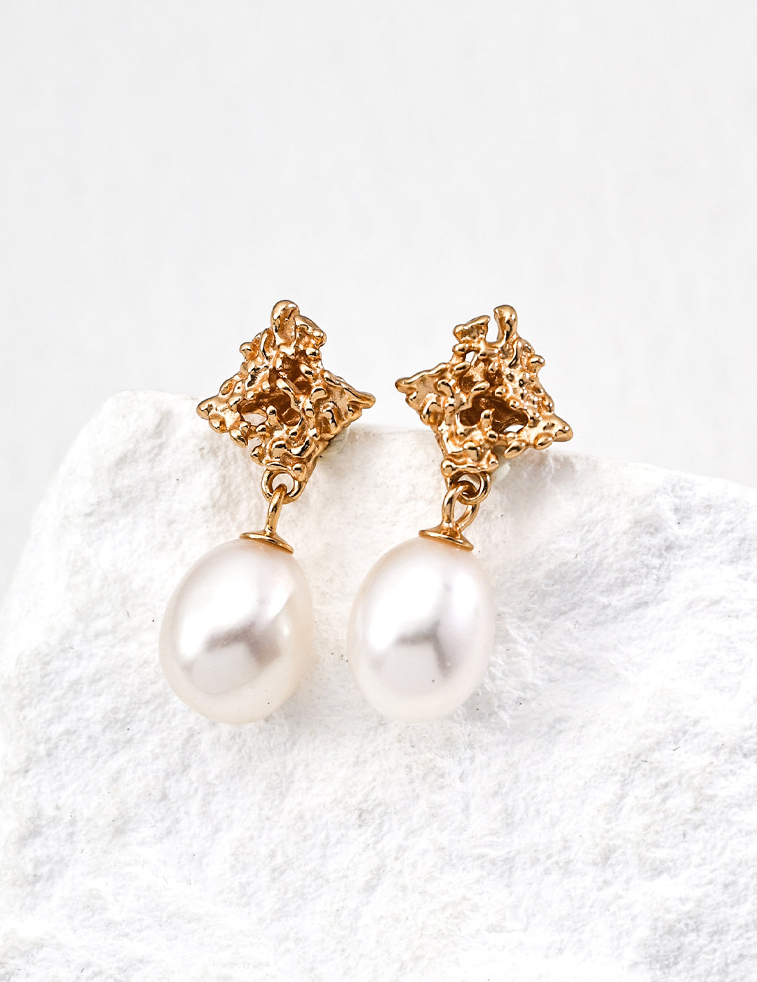 Elegant gold earrings with white pearls, featuring a unique sculptural style for a luxe look.