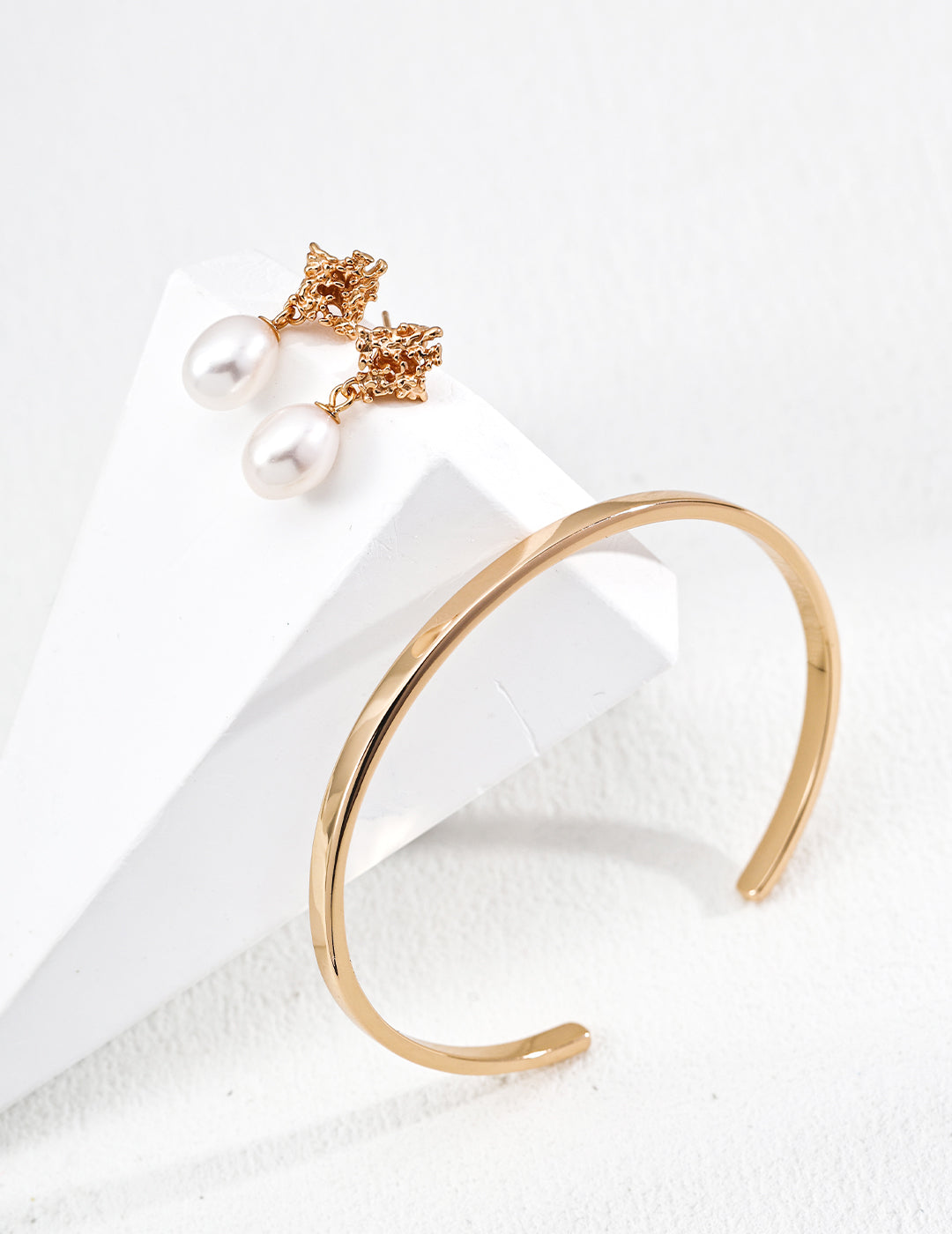 Stunning refined gold bangle and sculptural pearl earrings, radiating a chic and luxurious vibe.