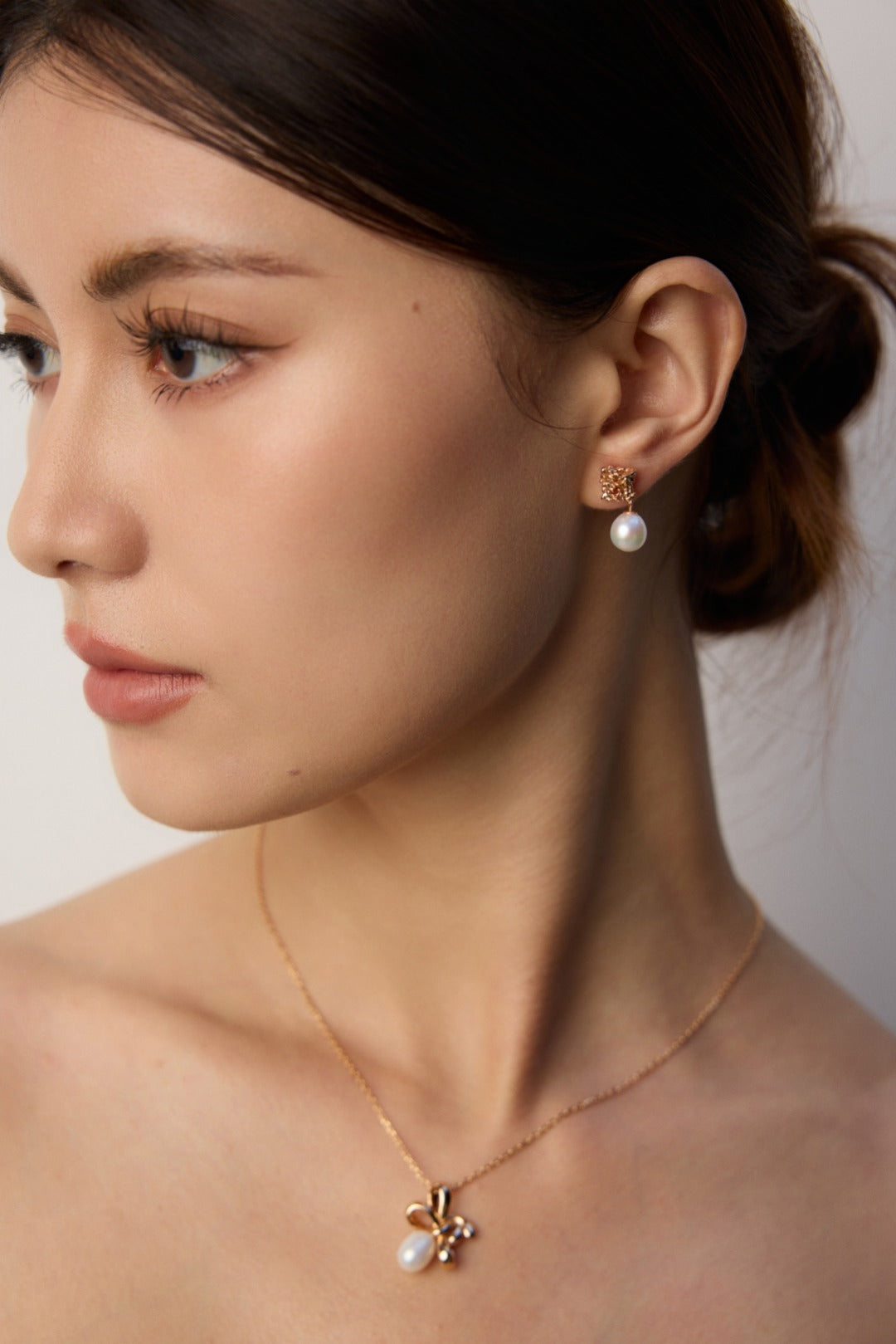 A woman with a gold necklace and stunning sculptural pearl earrings, radiating an air of effortless luxury.