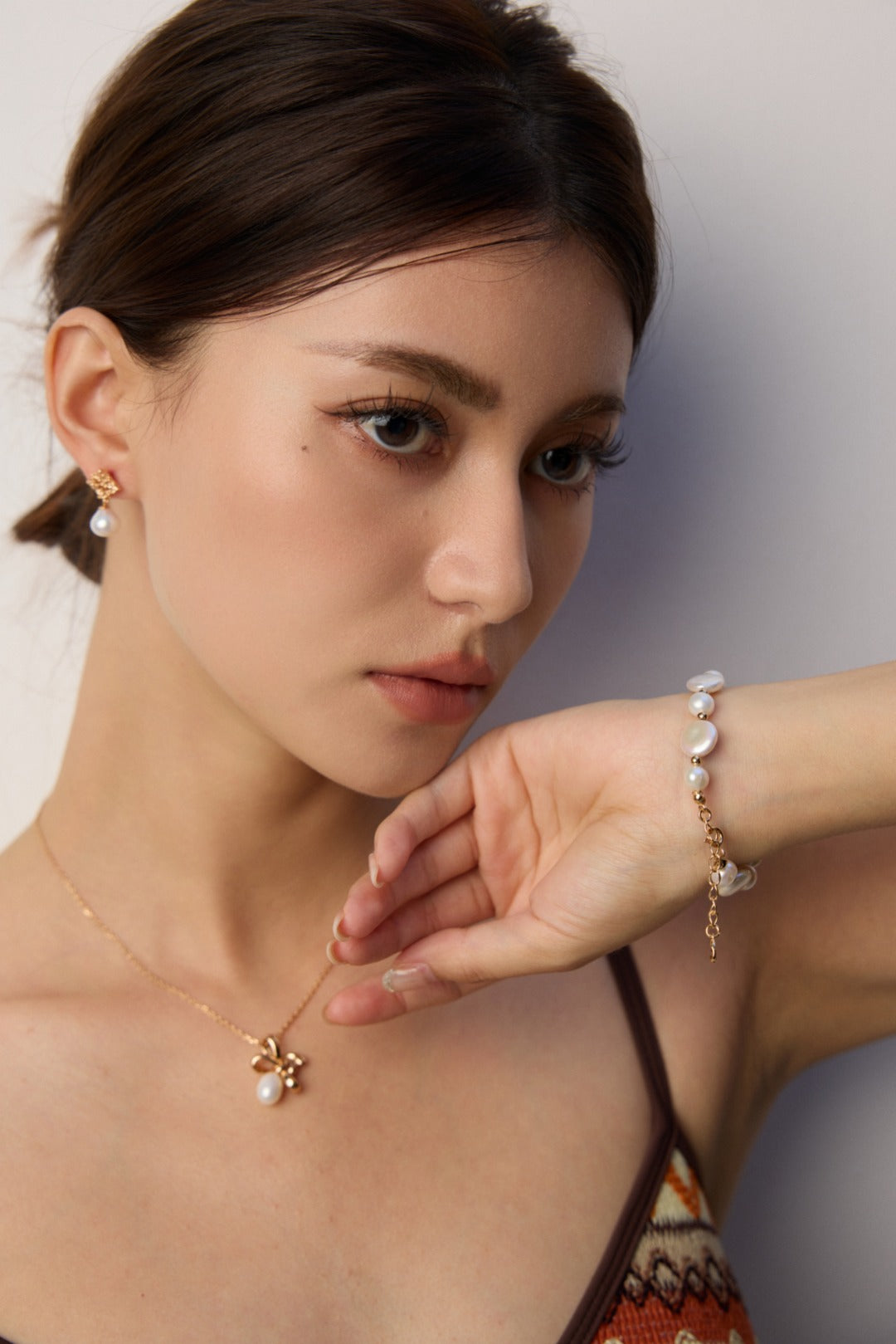 A woman adorned with a gold necklace and bracelet, featuring elegant sculptural gold pearl earrings from Mezuille.