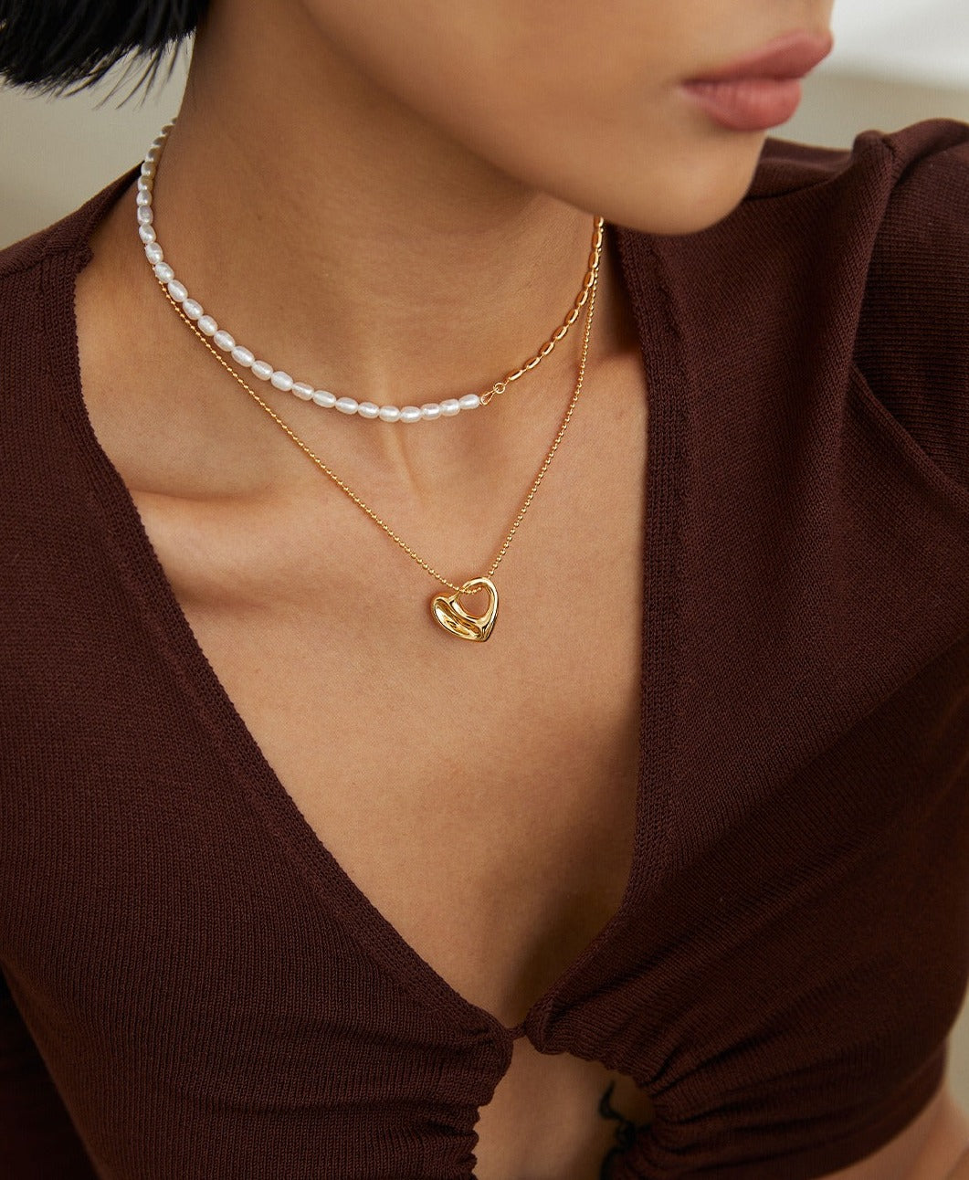 A woman wearing a gold necklace with a chubby heart charm, symbolizing love and affection.