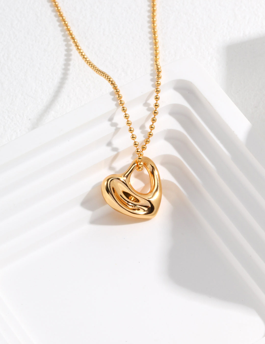 A gold chubby heart pendant necklace resting on a white plate.