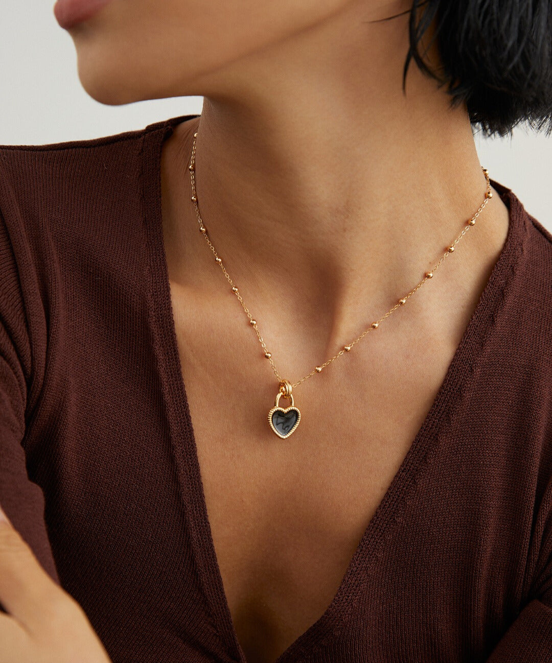 Woman in gold necklace with black enamel heart charm.