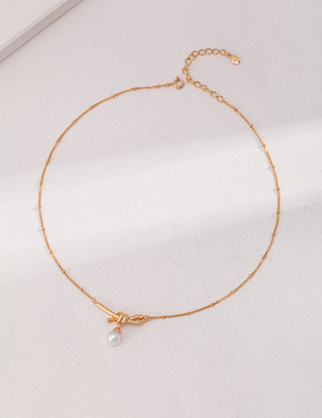 Elegant gold necklace with pearl knot charm.