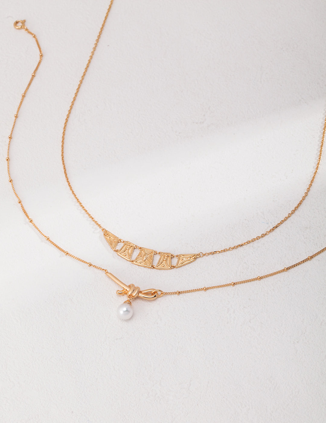 Gold necklaces with pearl knot and square pendants.