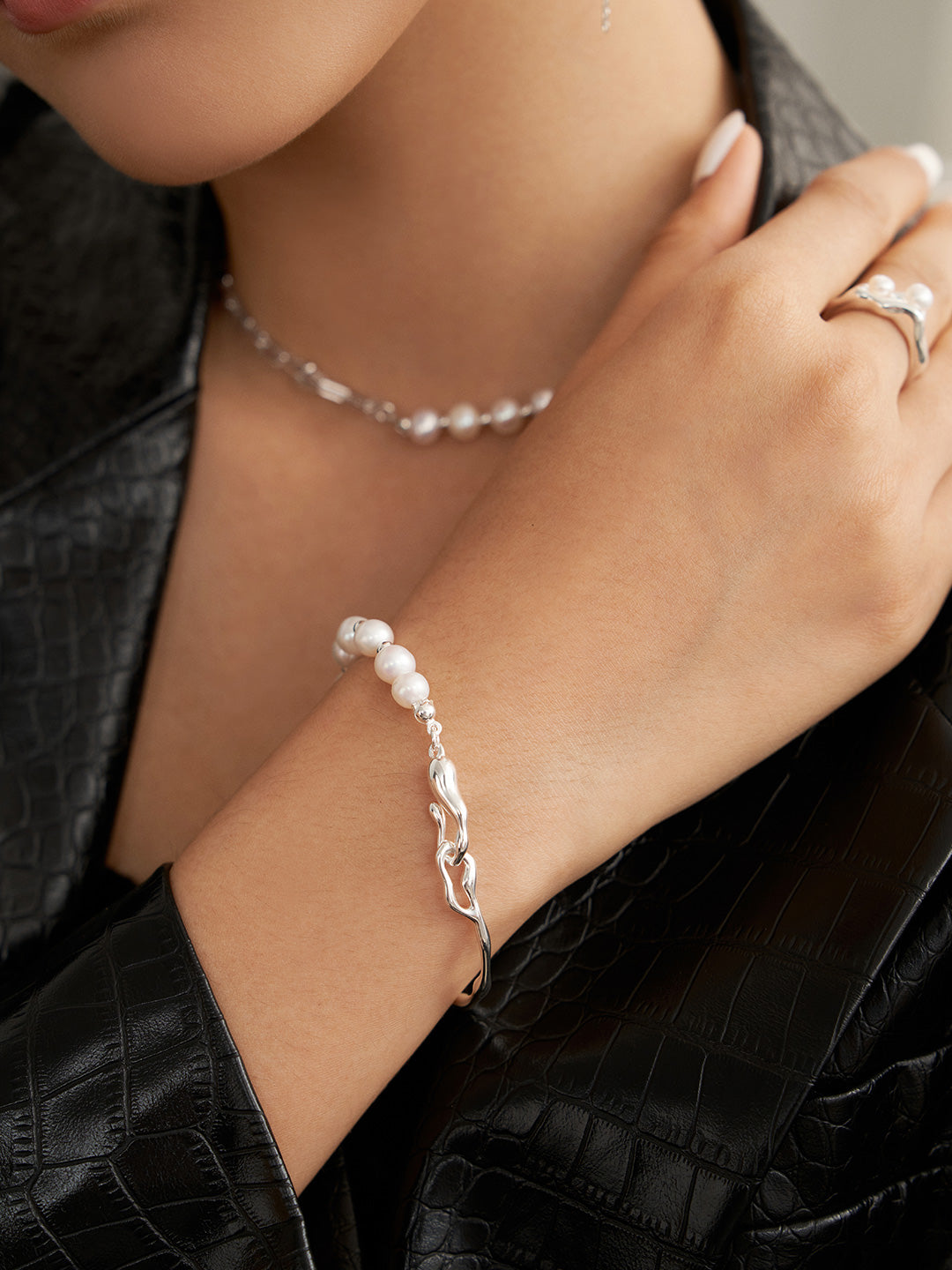 A woman wearing a silver bangle and a pearl necklace, model showcasing half silver bangle, half freshwater pearls bracelet.