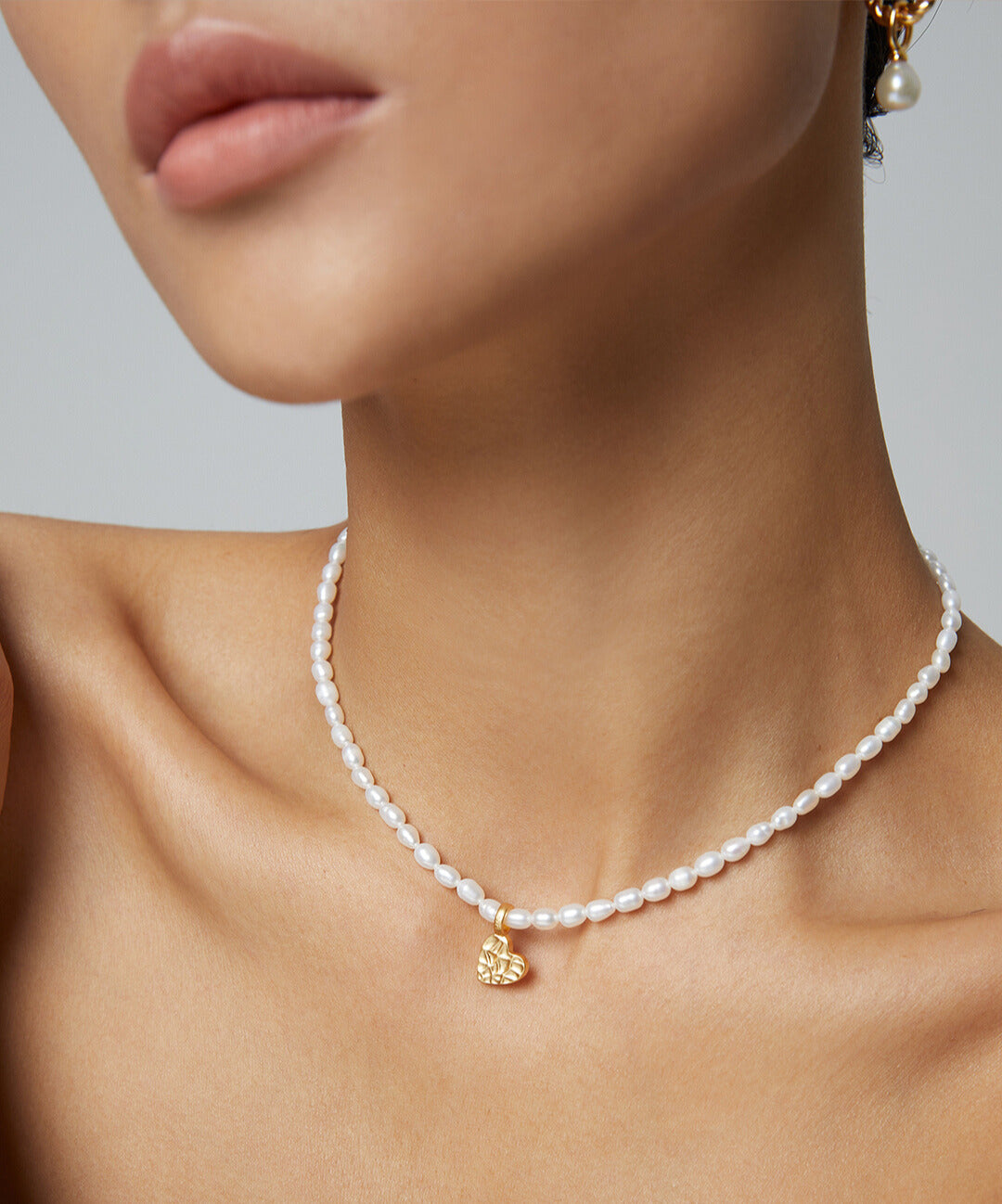 Woman in pearl necklace and gold earrings, with dainty pearl necklace featuring gold mini heart pendant.