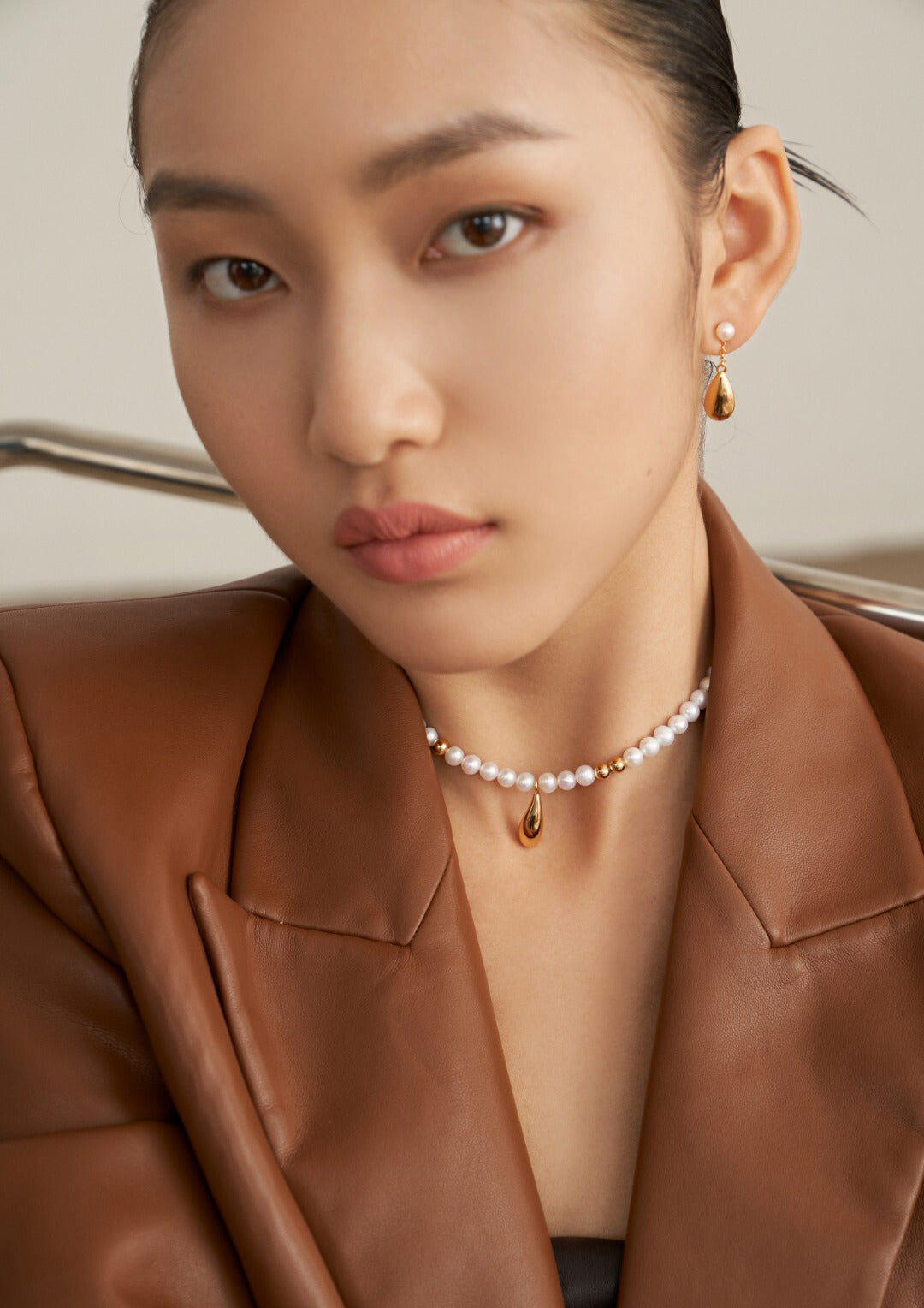 Model in brown jacket accessorized with gold and freshwater pearls necklace.