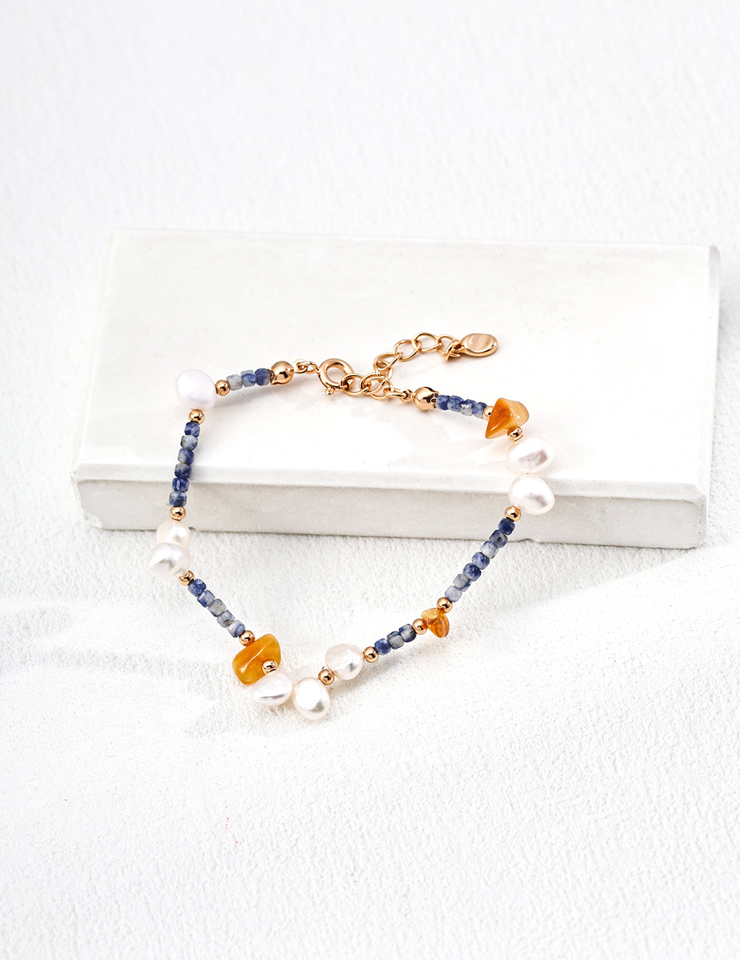 A colorful bracelet made of blue Azurite in Granite, orange beeswax beads, and freshwater pearls.