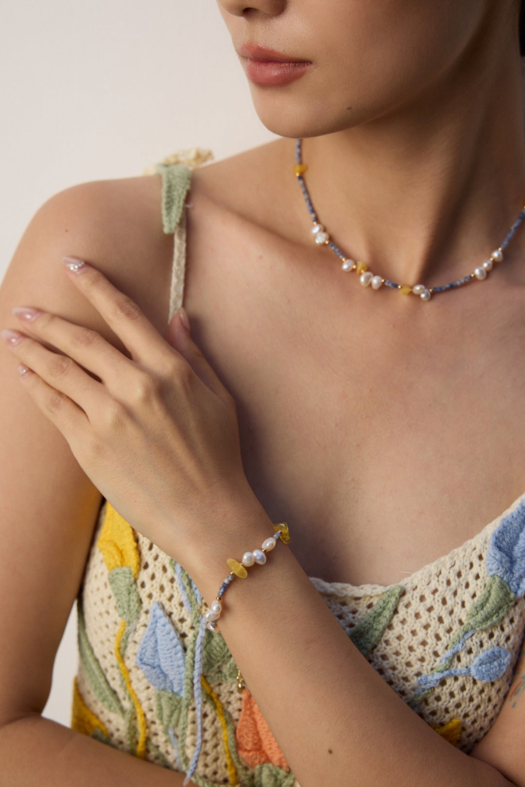 A woman showcases a yellow and blue necklace and bracelet crafted from Azurite in Granite, beeswax, and freshwater pearls.