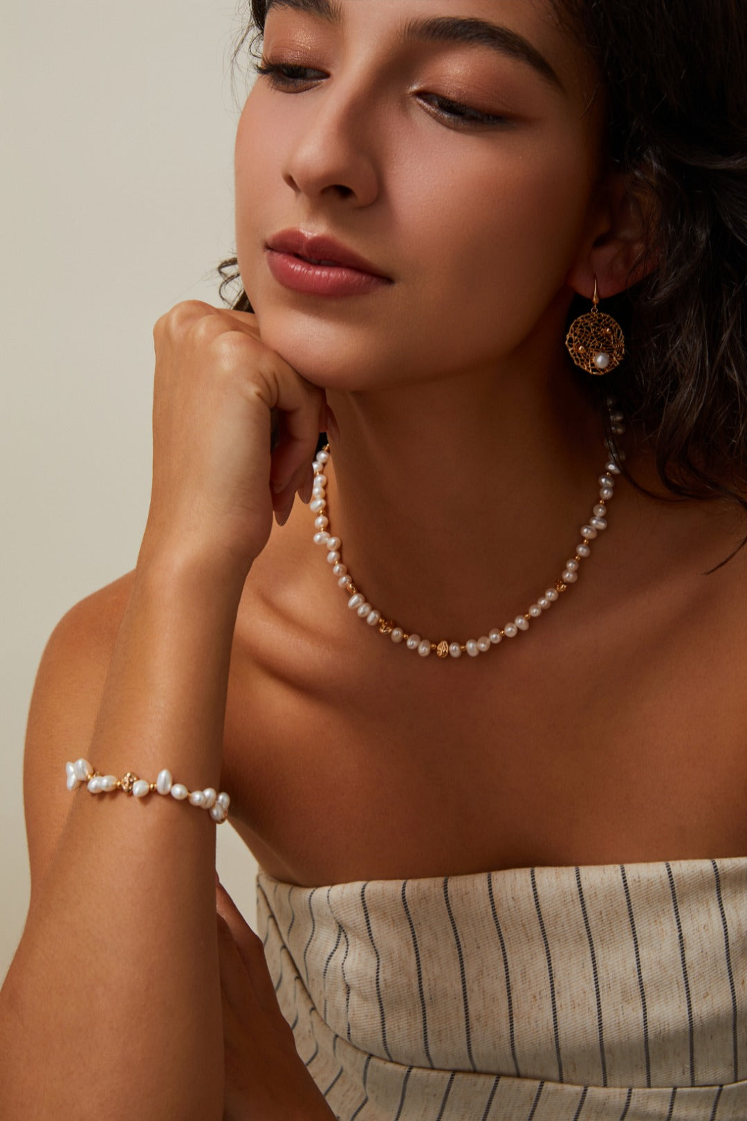 Lifestyle photograph of a model showcasing the Natasha pearl necklace, styled as a complete set with the matching pearl nugget bracelet and statement gold drop earrings.