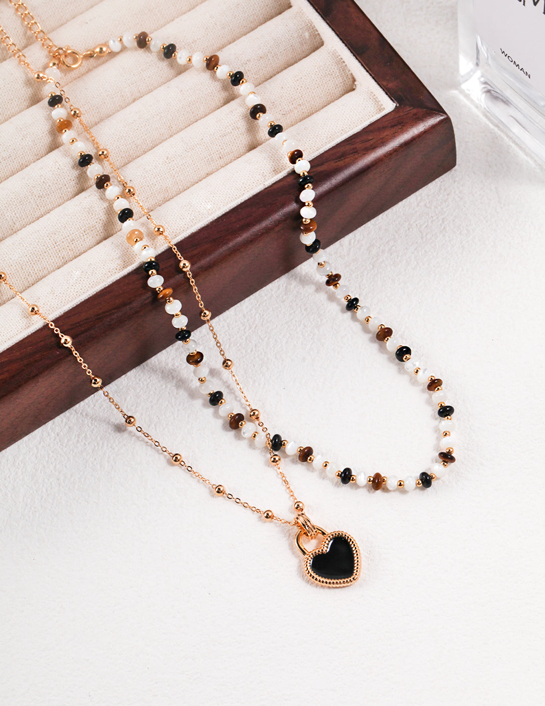 Wooden tray holding two gold plated necklaces with black and white beads.