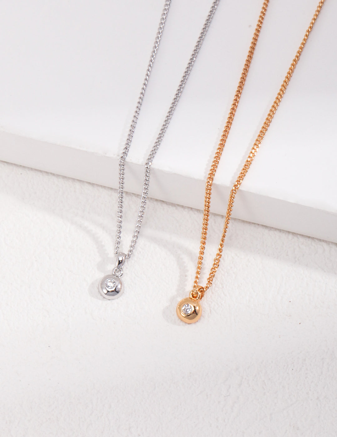 Two elegant chain necklaces, one in silver and one in gold, adorned with delicate cubic zirconia pendant.