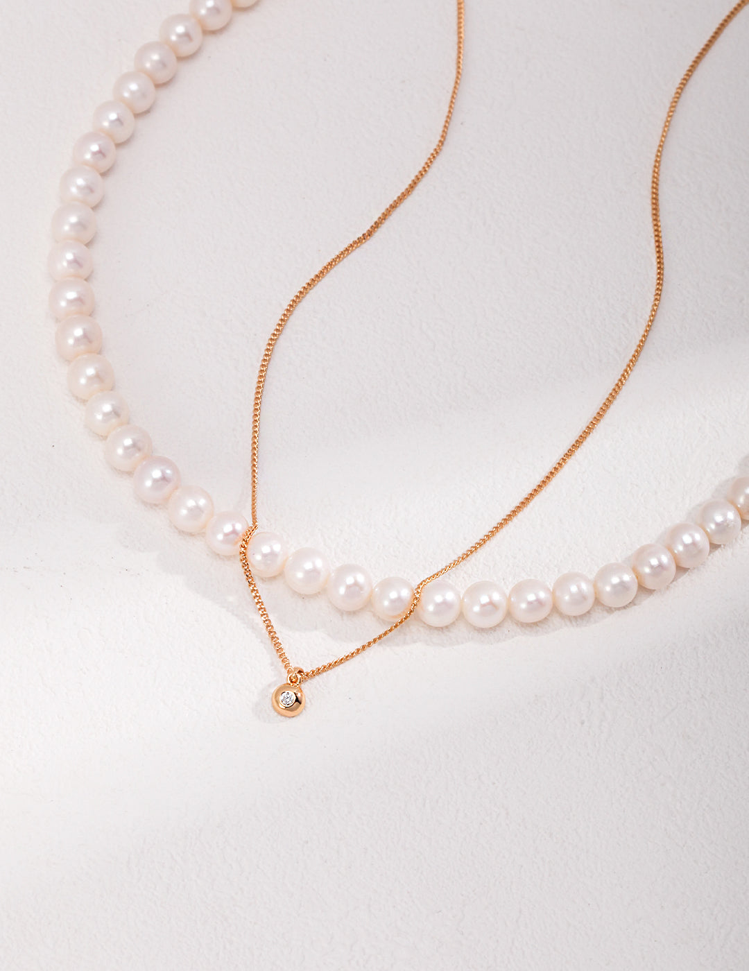 Elegant pearl necklace and a gold chain necklace with a cubic zirconia pendant.