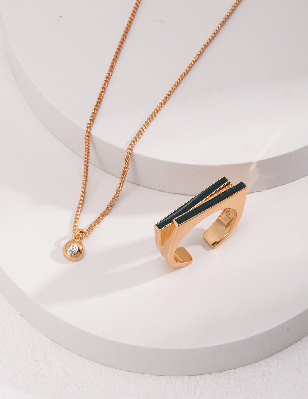 Gold chain necklaces with dainty cubic zirconia and an edgy ring on a white surface.