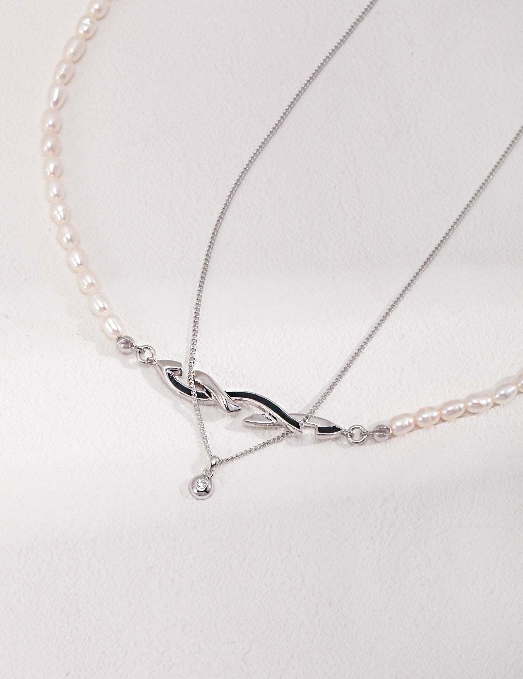 A silver chain necklace layered with pearl necklace, adding elegance to any outfit.