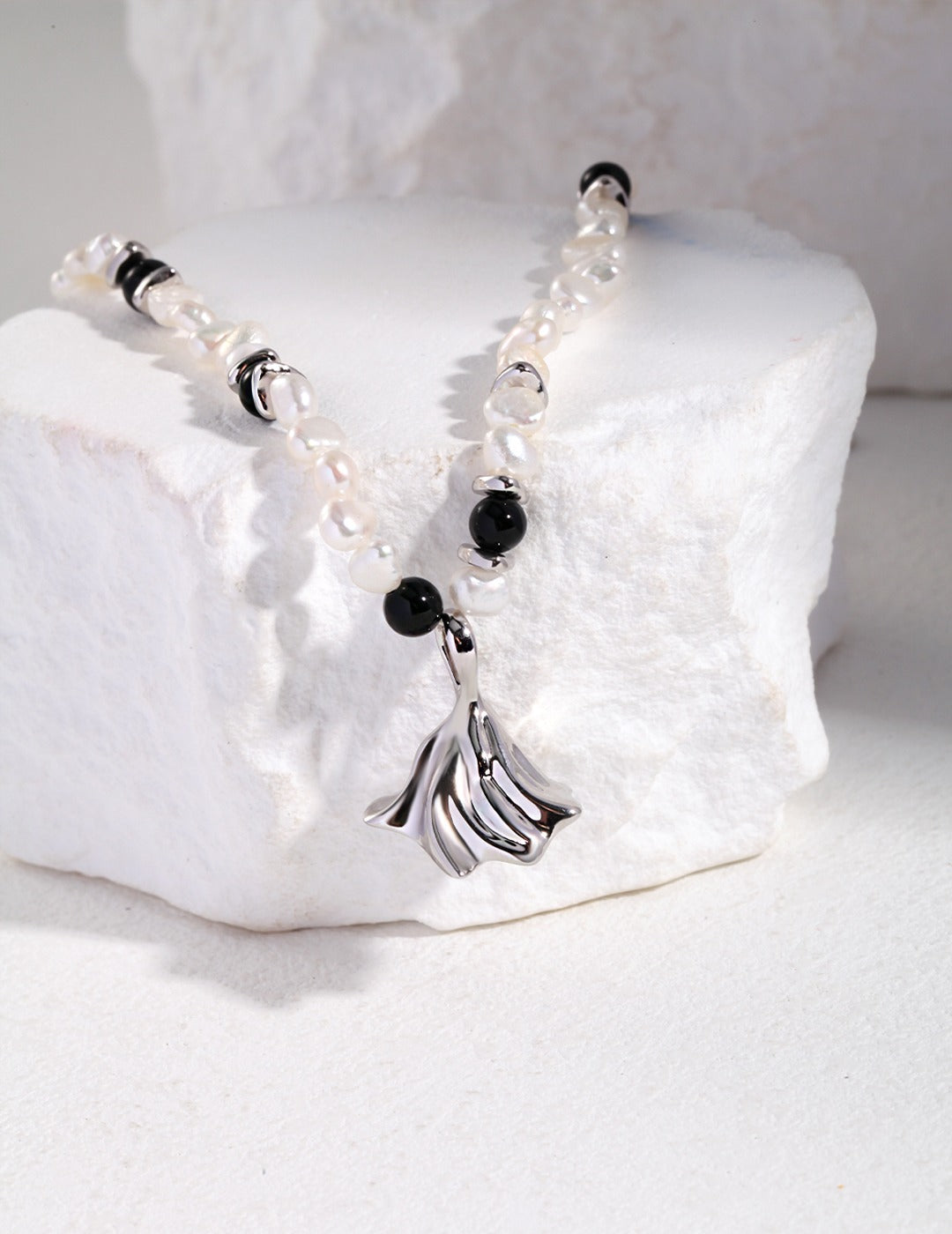Close up of silver charm pendant on white pearl necklace with agate and freshwater pearls.