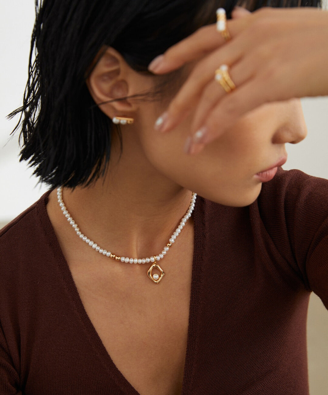 A woman wearing a gold charm necklace with freshwater pearls, adding elegance to her outfit.