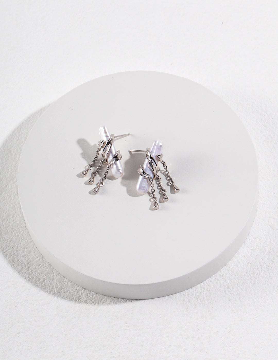 A pair of silver plated baroque pearl earrings, placed on a white plate.