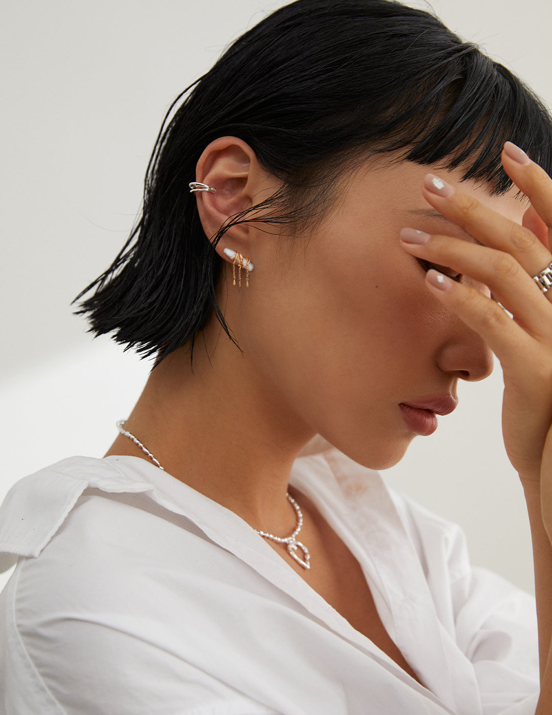 Short-haired woman in white shirt holding head, with gold plated baroque pearl earrings.