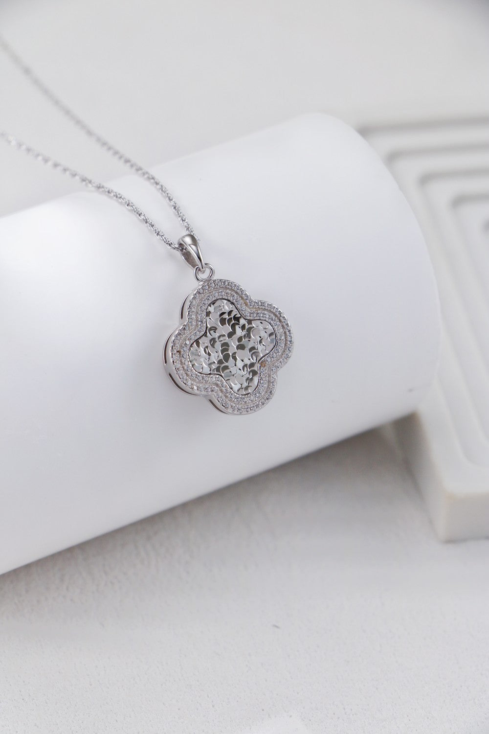 Close-up of a sparkling zirconia clover pendant on a white backdrop, highlighting its elegant floral design.
