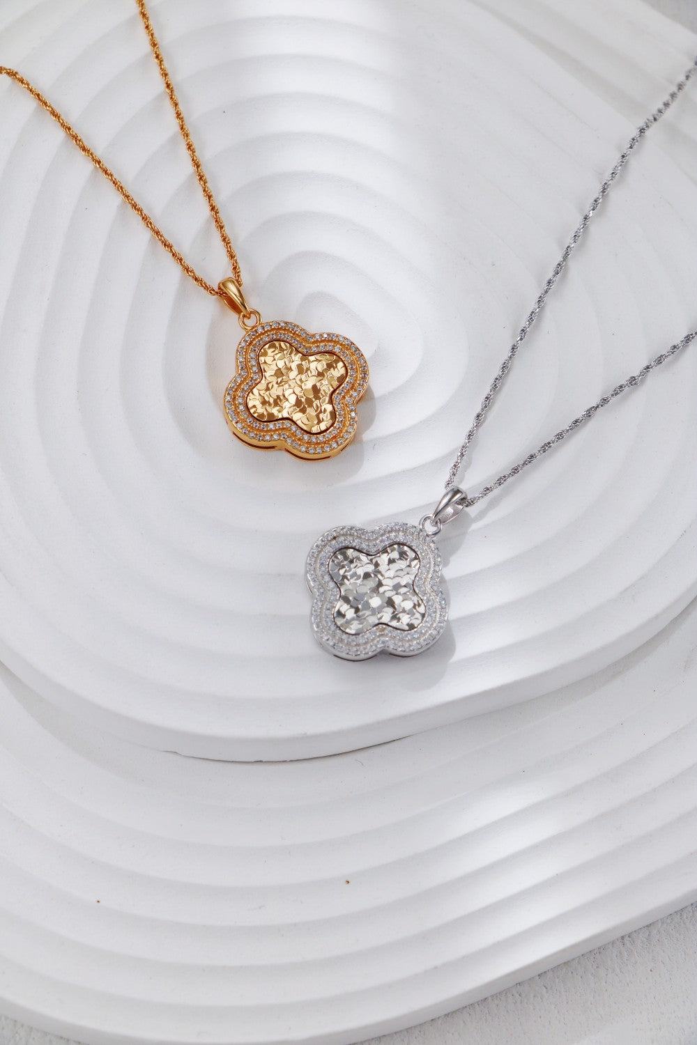 Two necklaces: one silver and one gold, both adorned with a zirconia pendant, showcasing a clover design.