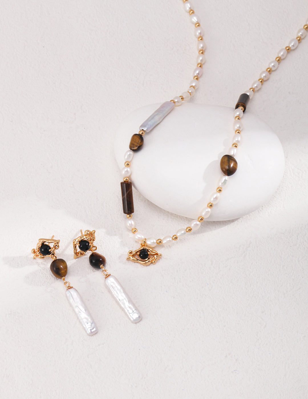 A stunning gold plated necklace and earrings set featuring a pearl necklace, tiger's eye stones, freshwater pearls, and a black agate pendant.