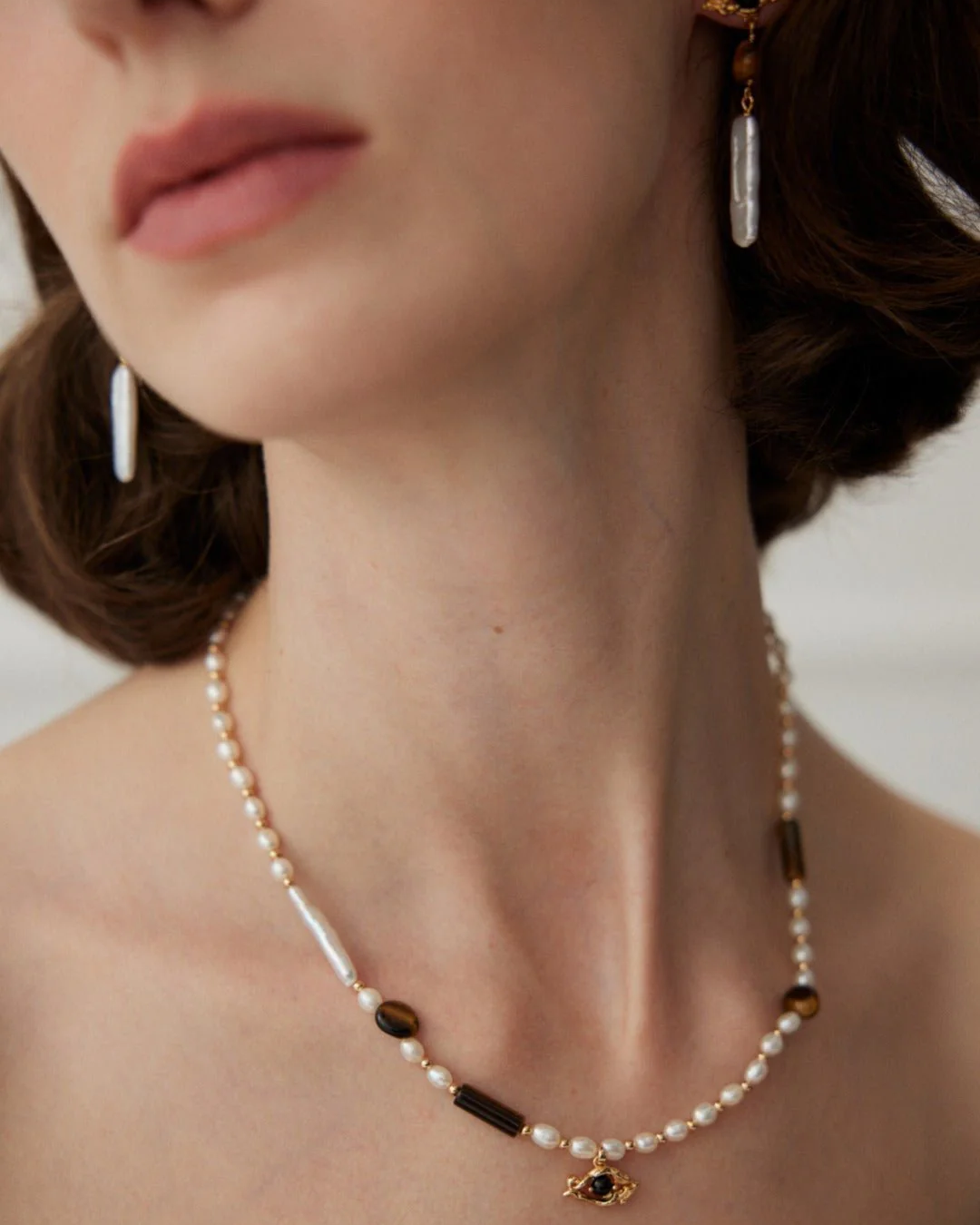 A woman wearing a pearl necklace with a gold chain, complemented by matchy tiger's eye and evil eye jewelry