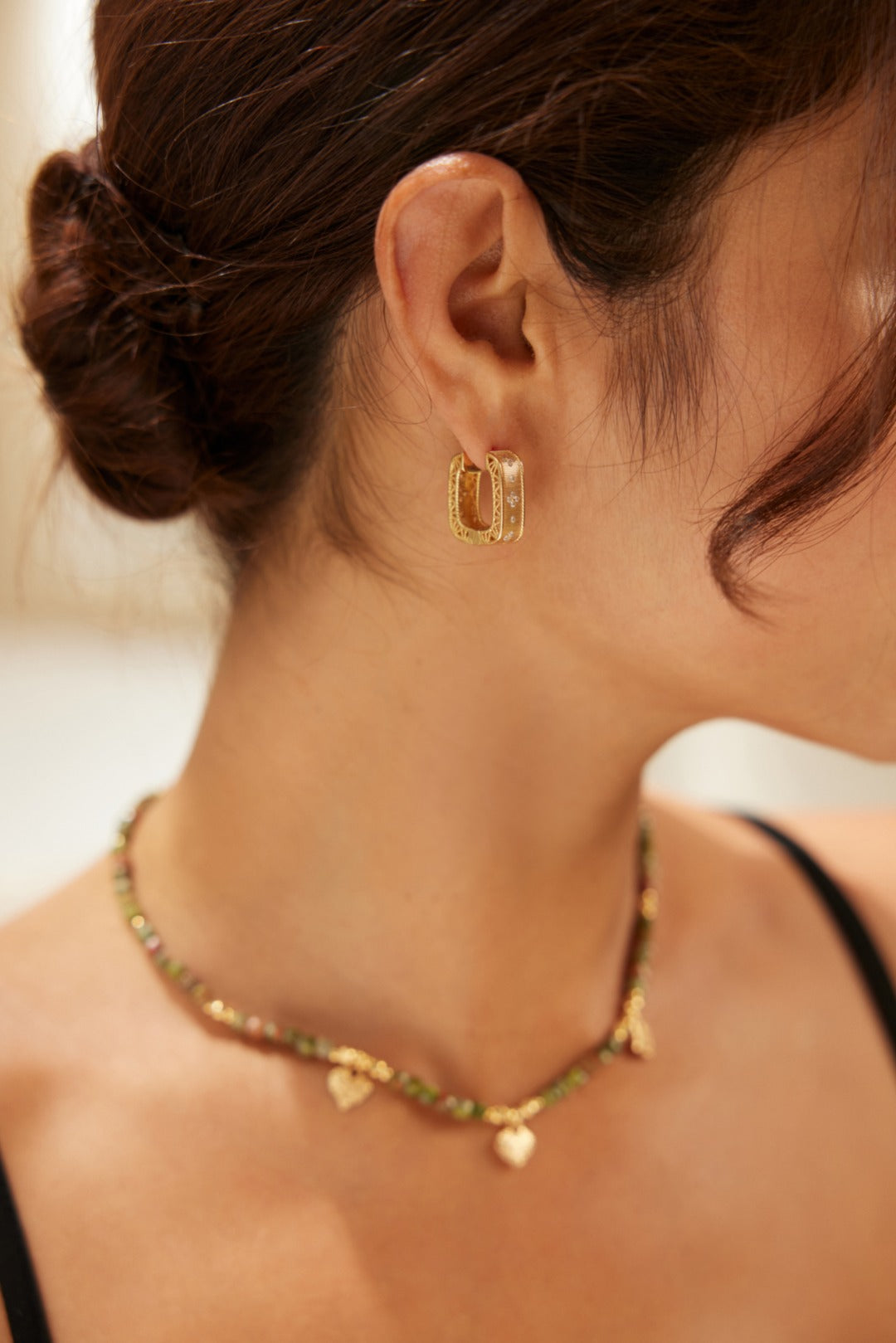 A woman adorned with a gold necklace and hoop earrings, radiating confidence and style.