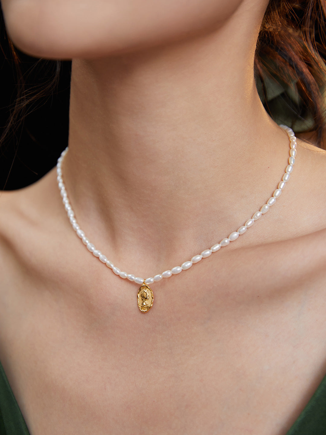 Woman wearing necklace with rice pearls and queen figure medallion.