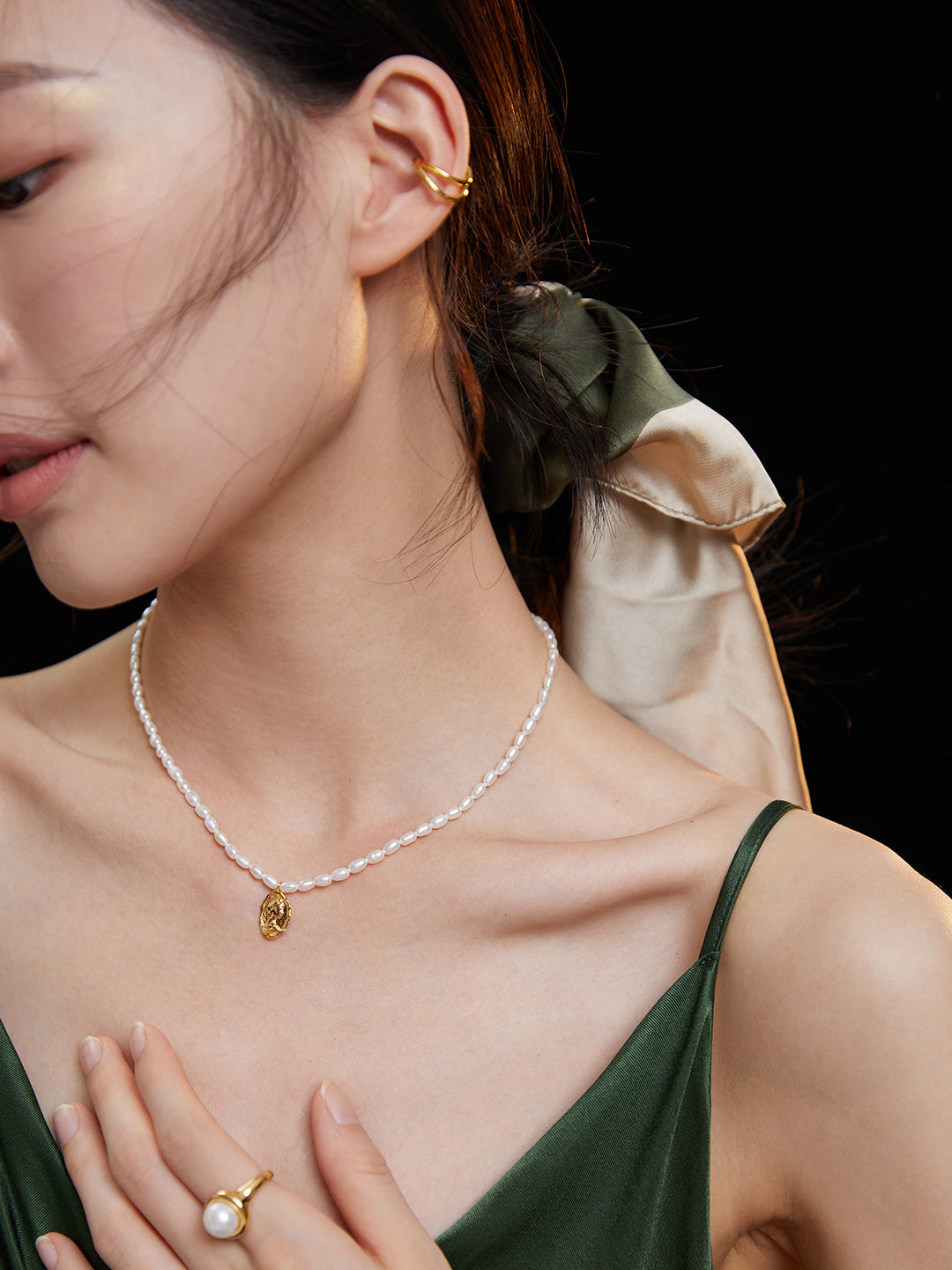 A stylish model in a green dress adorned with a necklace featuring rice pearls and a queen figure medallion.