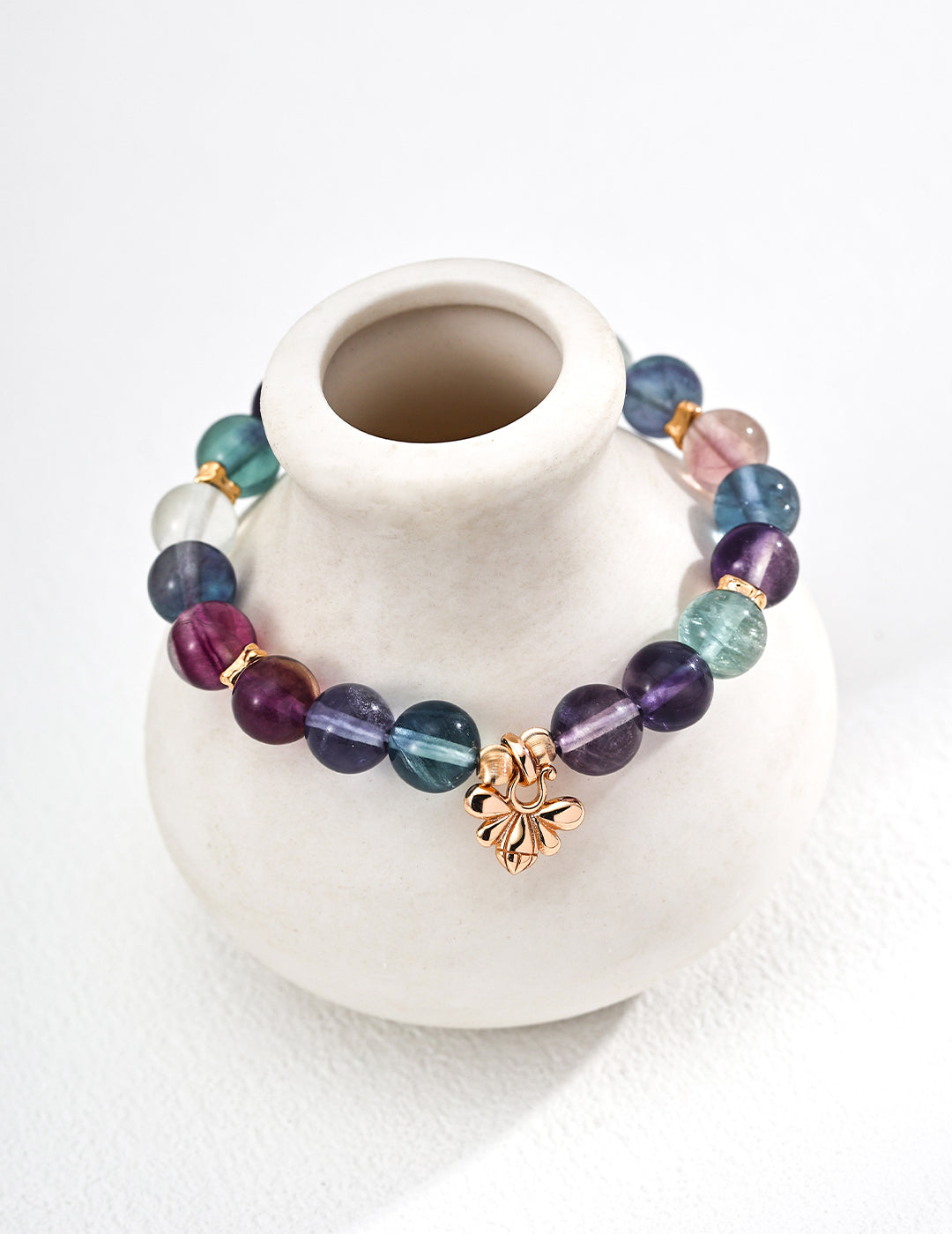 A white vase with a vibrant fluorite bracelet, adorned with an array of colorful stones in a striking combination.