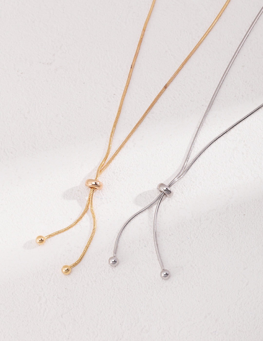 Pair of elegant silver and gold knot necklaces featuring delicate ball charms.