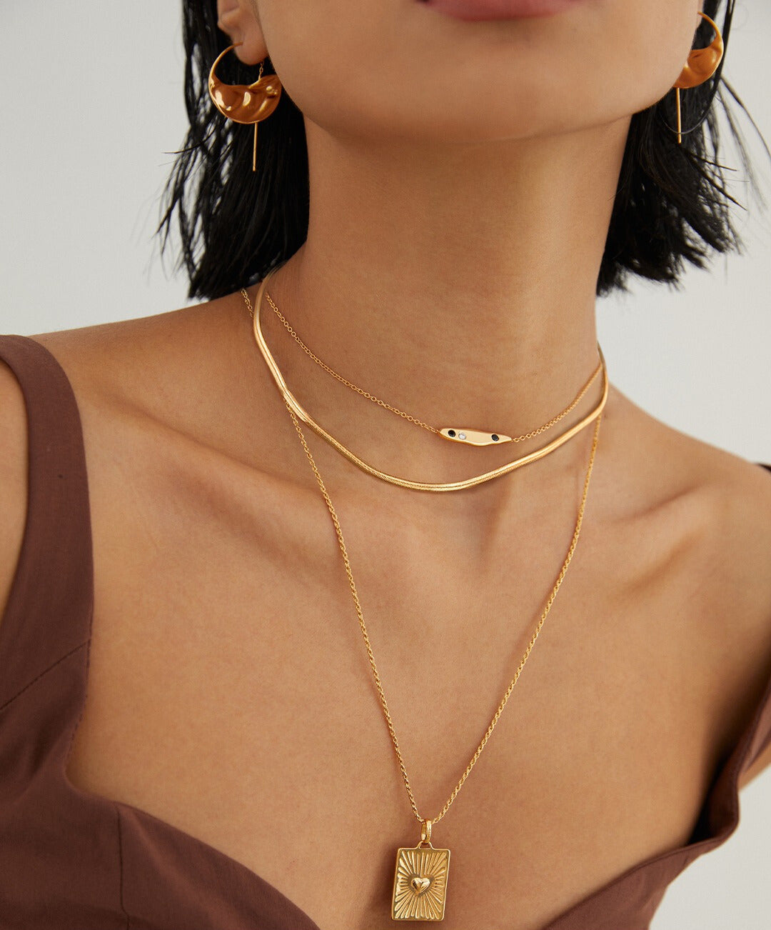 A woman wearing multiple gold plated necklaces, complemented by matching earrings.
